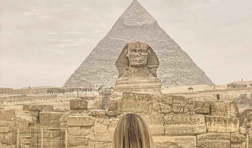 The Great Sphinx of Giza with its human face and lion’s body carved from limestone, standing beside the Pyramids under a bright sky.