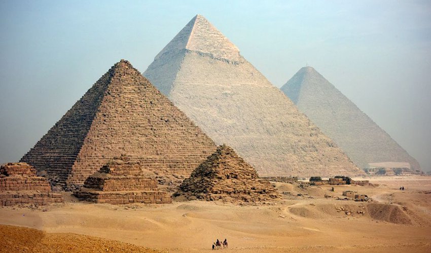 The Great Pyramids of Giza rising above the desert sands with the Sphinx in the foreground under a clear blue sky.